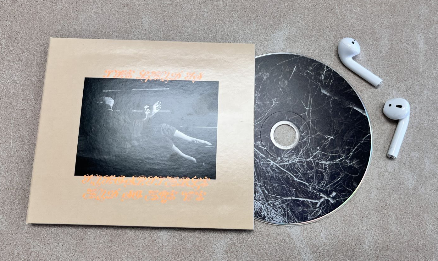 “The Land Is Inhospitable and So Are We” CD, which shows singer-songwriter Mitski on the floor, with the words “The Land Is Inhospitable and So Are We” around it.  The physical CD contains an image of trees.